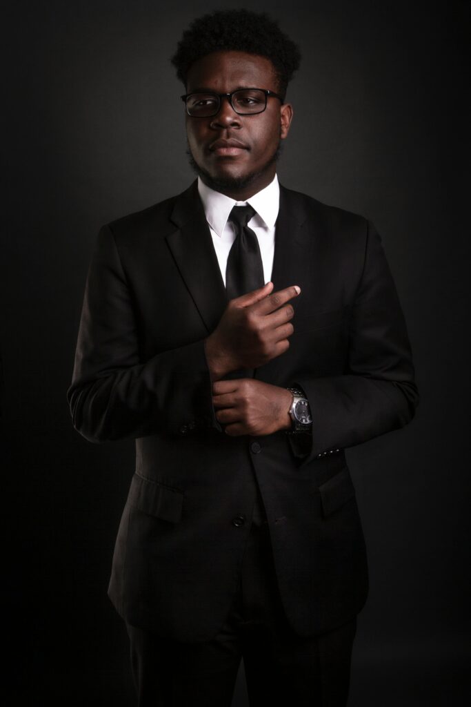 pexels-photo-2216607-2216607 Stylish African American man in a black suit, looking confident and professional against a dark background.